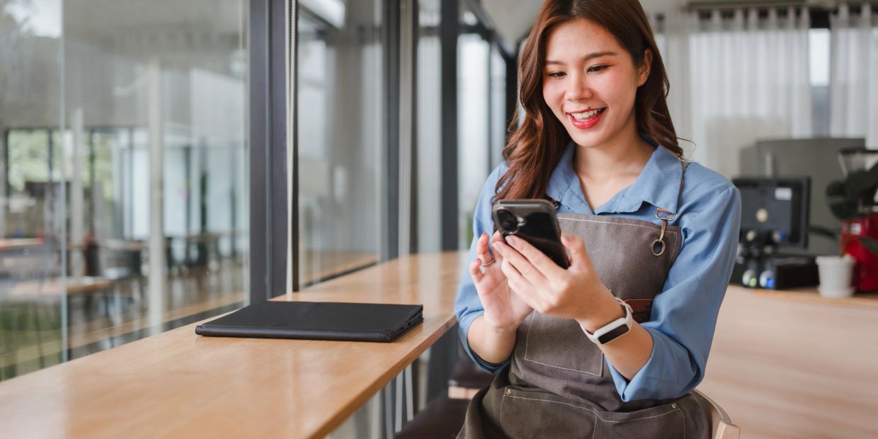 Woman in apron smiling at phone indoors.