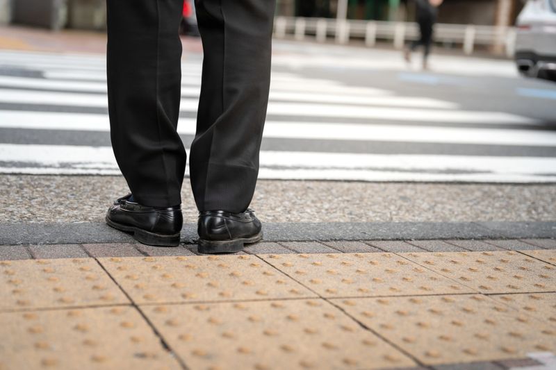 A businessman in black court shoe and slack trouser, formal working uniform, is waiting to crossing the road at zebra way. People and city life for transportation scene, close-up at low angle.