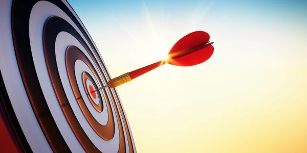 A dart hitting the bullseye on a target against a bright sky.