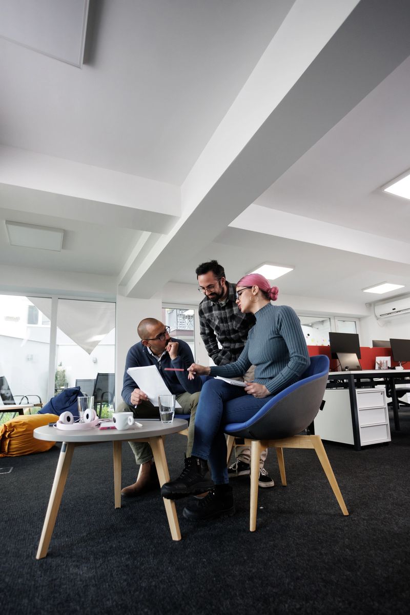 Businesspeople engage in a collaborative discussion in a contemporary office space. They share ideas while reviewing documents and using digital devices at a coffee table.