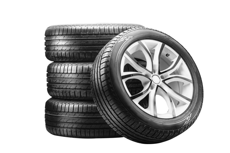 Four summer tires mounted on alloy wheels are neatly stacked, showcasing their design and tread. This setup highlights seasonal tire service and sales opportunities