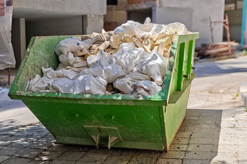 Industrial Dumpster Full of Construction Debris and Rubble on Urban Street. Building Renovation Waste Management and Cleanup Concept