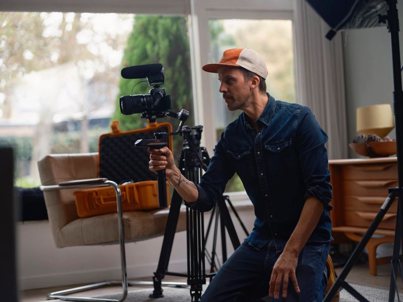 Videographer kneeling while operating camera gimbal capturing smooth footage in bright studio workspace