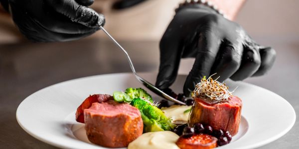 Chef garnishing a plated gourmet dish with black gloves.