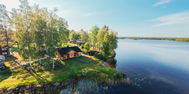 Cabins by a calm lakeside surrounded by trees and greenery.