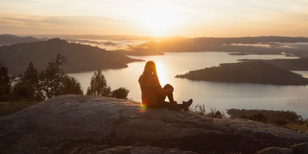 Person sitting on a rock watching the sunrise over a lake and hills.