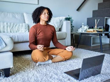 A woman meditating in her living room with a laptop in front of her.