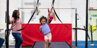Children playing and swinging on gymnastic rings with adult supervision.