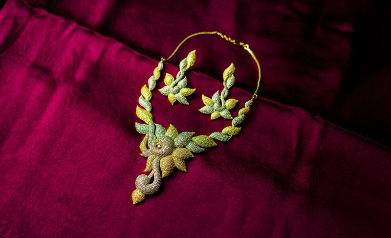 Exquisite handmade necklace with earrings in gold tones placed artistically on a rich velvet background.