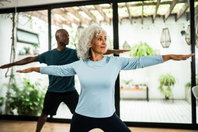 Older couple doing yoga poses indoors.