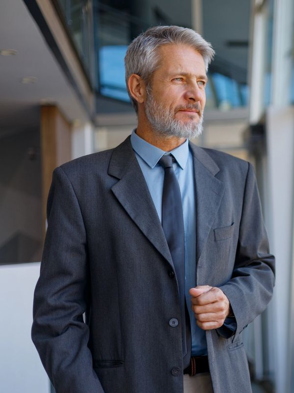 A confident older man in a suit gazes thoughtfully out a window.