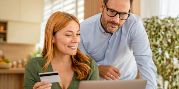 A woman holding a credit card, with a man looking at a laptop together.