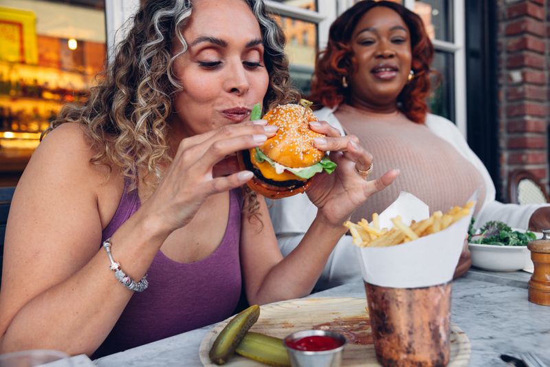 Two smiling women are seated at a stylish café, indulging in a delicious meal and lighthearted conversation, representing friendship, leisure, and modern dining culture.