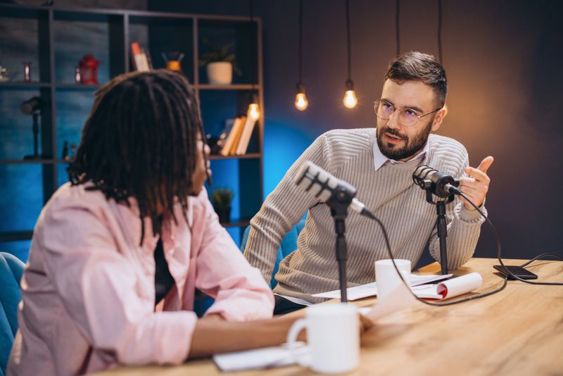 Two podcasters engaging in a lively discussion during a live recording session in a professional studio, surrounded by advanced audio equipment