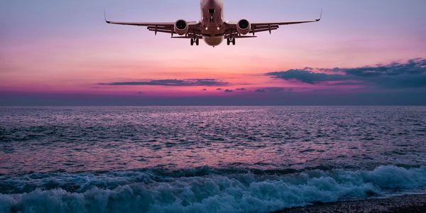 Airplane flying over ocean during sunset.