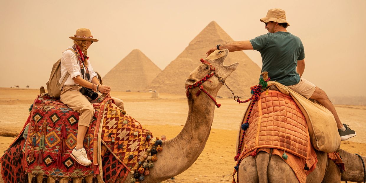 Two tourists riding camels near the pyramids.
