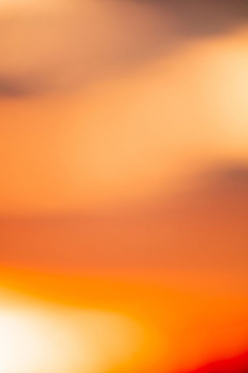 Vibrant, abstract gradient background featuring warm tones of orange, yellow, and a hint of purple, with a soft, natural bokeh effect, ideal for backgrounds or overlays