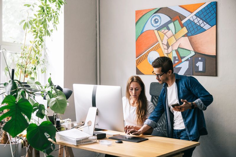 A modern workspace with two creative individuals collaborating on a project, showcasing teamwork and productivity. The room features bright lighting, a contemporary design, and artistic decor, fostering a dynamic atmosphere.