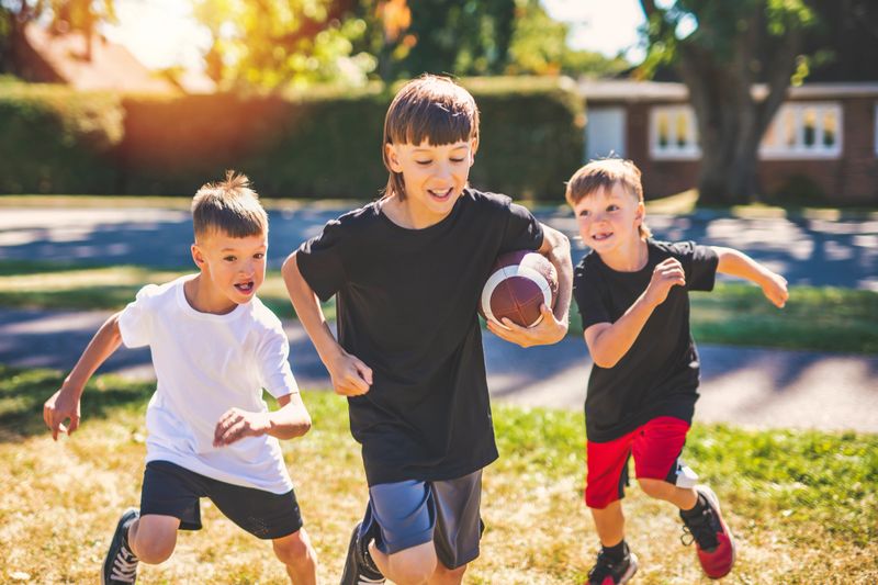 The brother playing American football. Kids play football in sunny summer park.