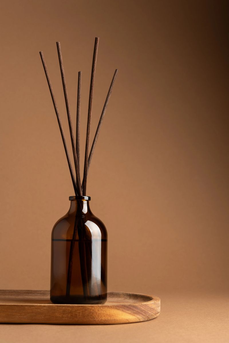 Amber glass aroma diffuser with brown reeds on a wooden tray, minimalist product display on neutral background. Concept of relaxation, balance and natural home fragrance.