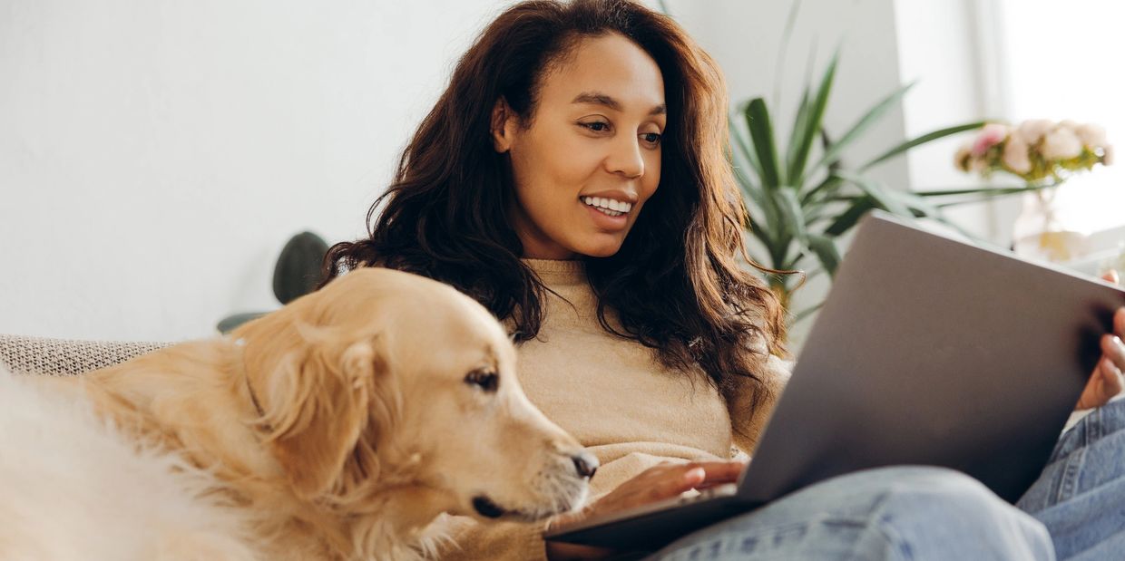 Woman using laptop with golden retriever beside her.