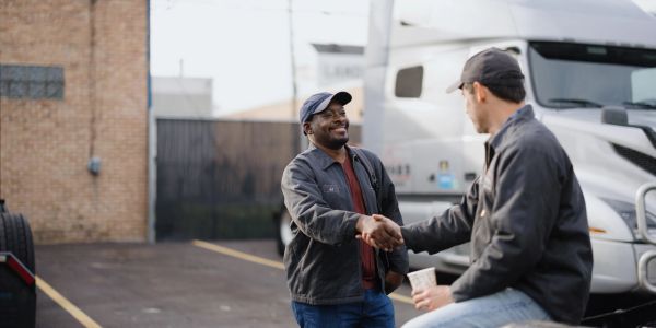Two truck drivers shaking hands in a parking lot.