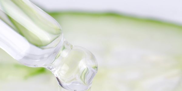 Dropper releasing clear serum on cucumber slice for skincare.