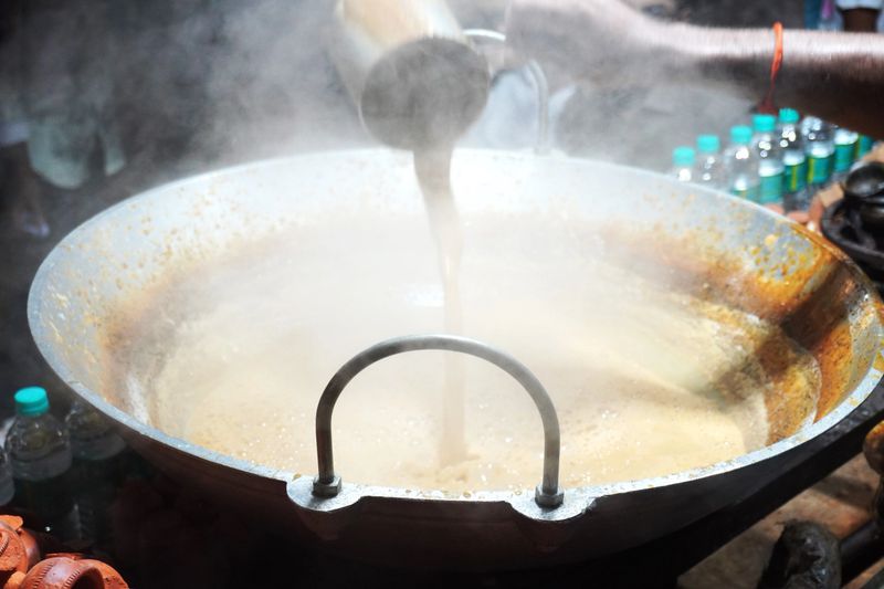 Large steaming kadhai of boiling masala chai being poured and prepared at Indian street tea stall