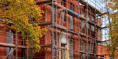 Scaffolding set up around a red brick building under renovation in autumn.