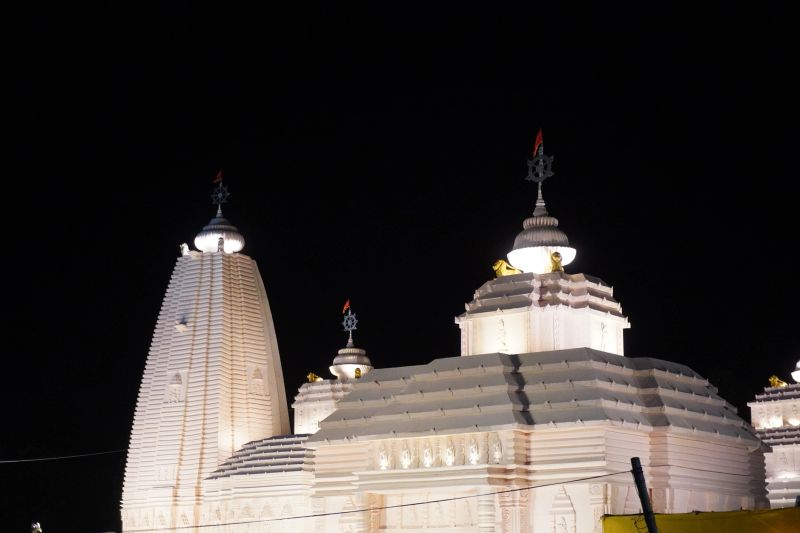 Illuminated white Hindu temple tower and domes against black night sky in India
