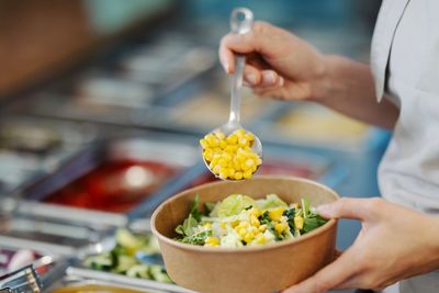 Person adding corn to a salad bowl at a salad bar.