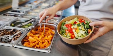 Nutritious meals - Person preparing a fresh salad at a salad bar with various vegetable toppings.