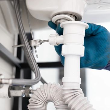 Gloved hand fixing a white plastic drain pipe under a sink.