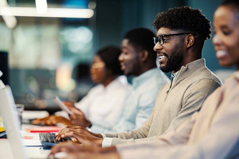 Group of diverse black business professionals collaborating and typing on computers during a busy workday in a contemporary office
