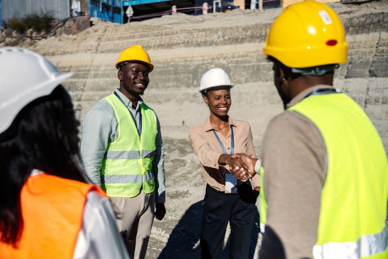 Diverse team of construction engineers building professionals shaking hands at a busy construction site