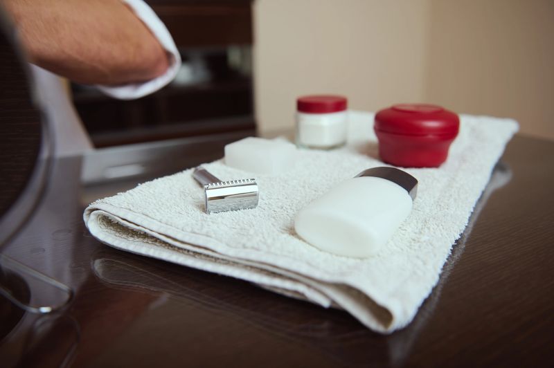 A tidy grooming set laid on a white towel, featuring a razor, shaving cream bottle, soap, and containers. Fresh, clean, and organized scene for grooming or men's care themes.