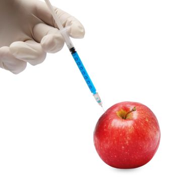A syringe injecting blue liquid into a red apple held by a gloved hand.