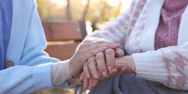 Two people holding hands outdoors, showing care and support.