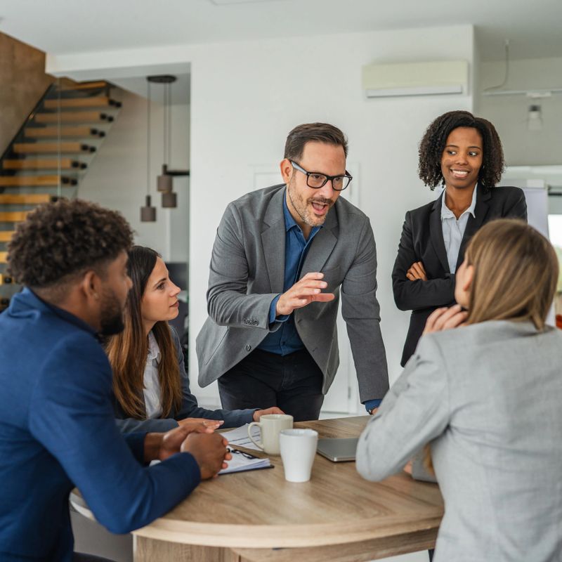 Diverse group of business professionals collaborating and discussing new ideas during an informal meeting in a contemporary office setting, showing teamwork and communication