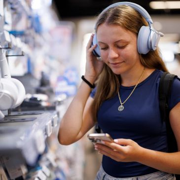 Young woman trying wireless headphones while checking her phone in a store.