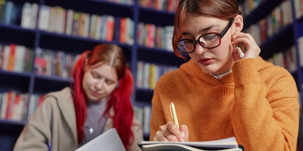 Two young women studying with notebooks in a library.