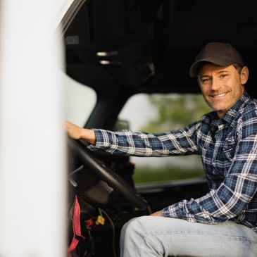 Smiling man in a plaid shirt driving a vehicle.