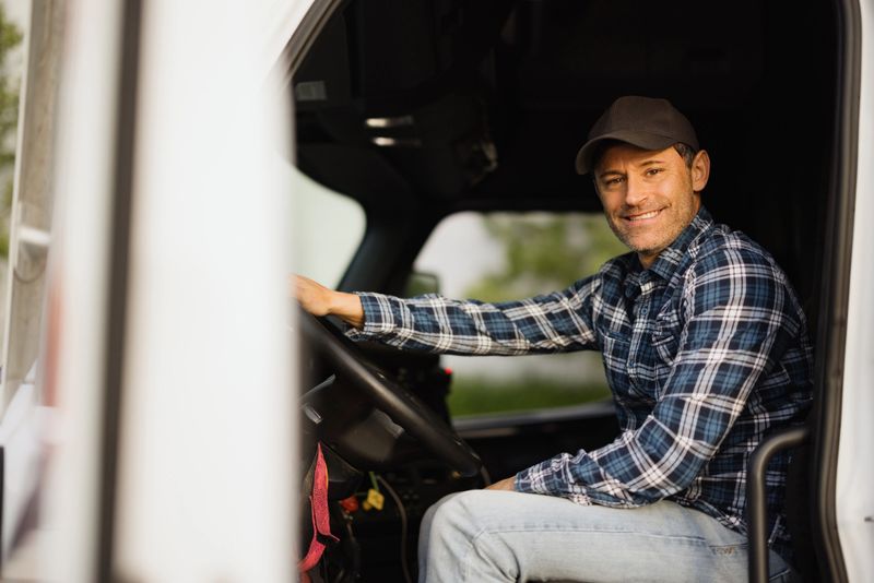 Portrait of a smiling truck driver sitting in his truck, holding the steering wheel and looking at camera