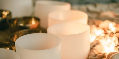 White crystal singing bowls arranged with warm lights and cozy textiles.