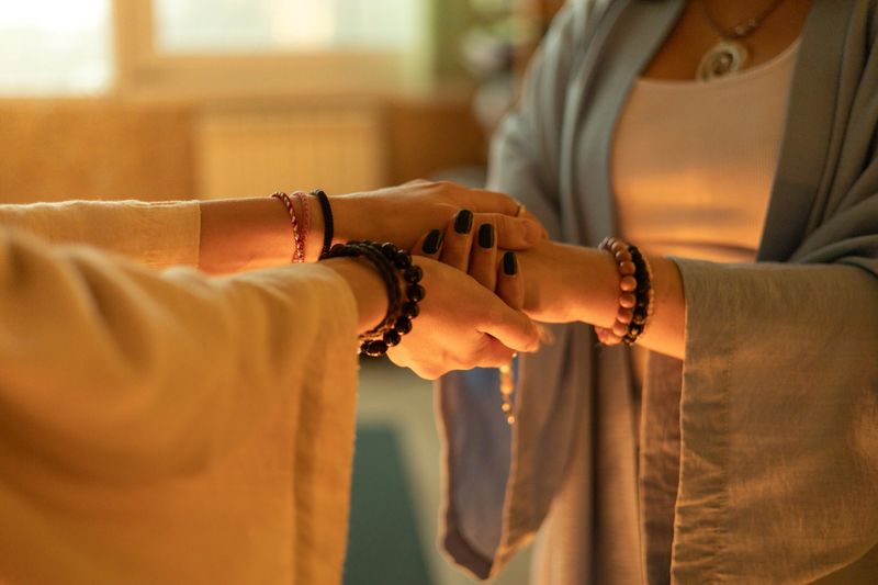 Women hold hands with focus and trust, symbolizing connection, grounding, and feminine energy. The image conveys calm, healing, and mindfulness in a sacred, peaceful atmosphere.