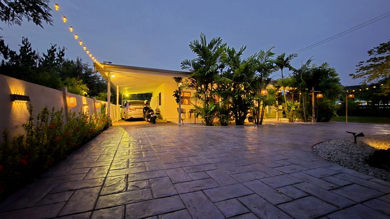 A serene residence in Thailand showcases modern stamp concrete architecture, surrounded by tropical plants. Soft lights illuminate the driveway as dusk falls,