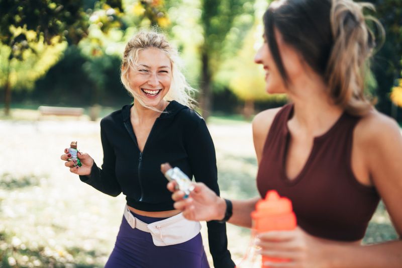 Two fit friends walking together in a park after exercising, smiling and enjoying protein healthy bars. The scene captures post-workout camaraderie and the importance of nutrition and friendship in fitness routines.