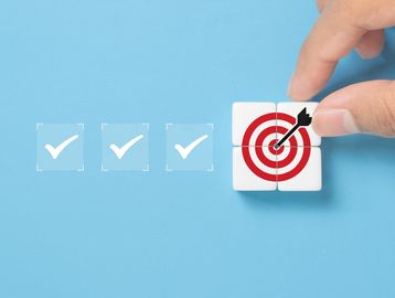 Hand placing blocks forming a bullseye target with check marks on blue background.