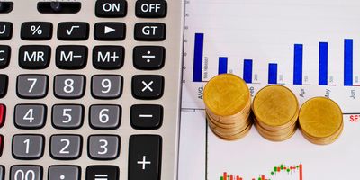 Calculator with stacked coins on financial charts.