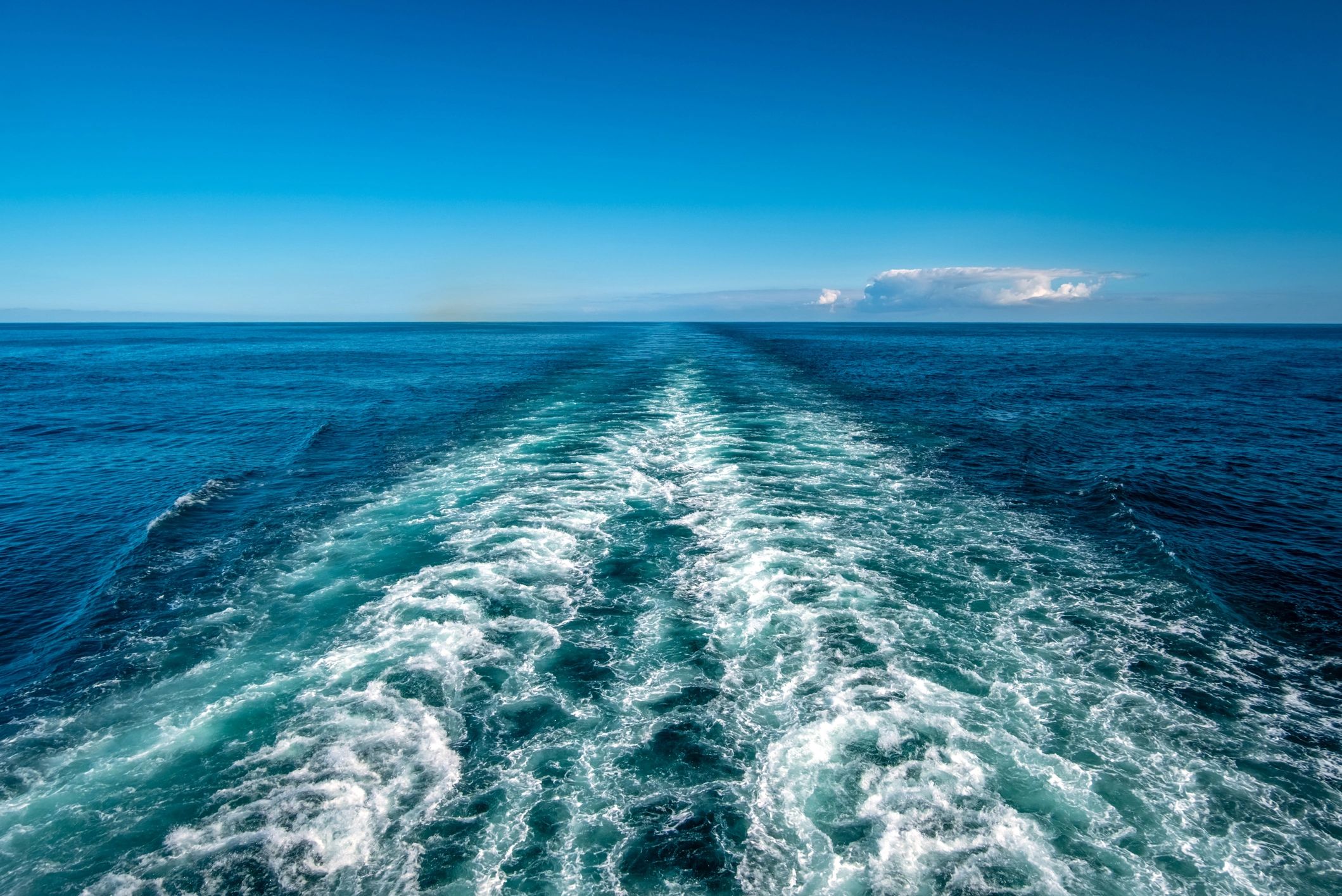 Wake trail in the ocean under a clear blue sky.
